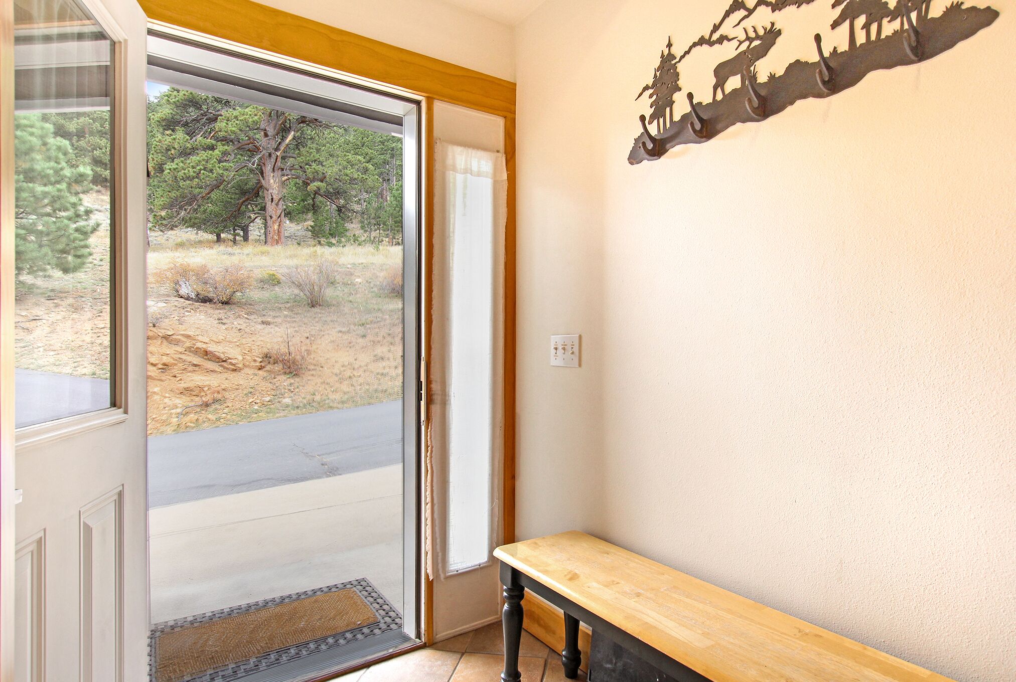 A room with a bench, a door leading to a view of trees, and a wall-mounted decoration.