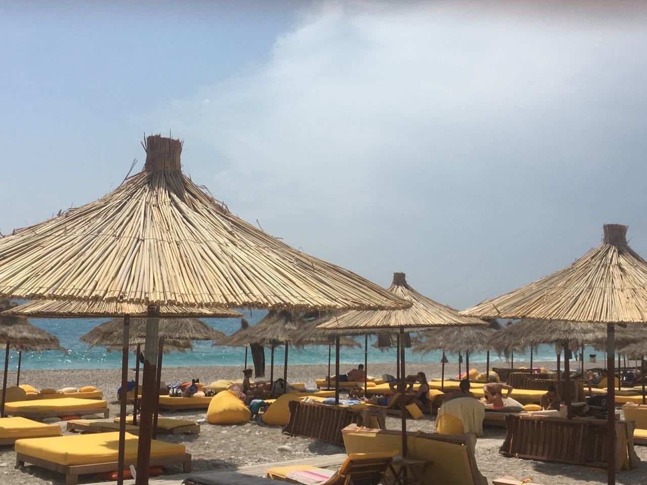 A beach with thatched umbrellas and yellow lounge chairs.