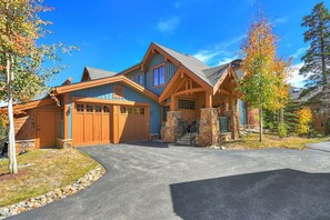 Stunning log cabin-style home with a central entrance and covered porch, set amidst a beautifully manicured lawn and stone retaining wall.