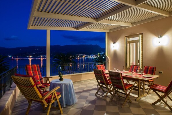A terrace with a table and chairs, a view of the sea, and a mountain in the background.