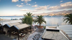 Een terras met buitenmeubilair, palmbomen en uitzicht op zee en bergen.