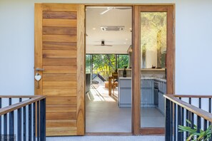 Une porte en bois donne accès à une cuisine moderne avec vue sur un jardin.