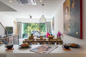 Un espace repas moderne avec vue sur l’extérieur, un ventilateur de plafond et un grand tableau abstrait accroché au mur.