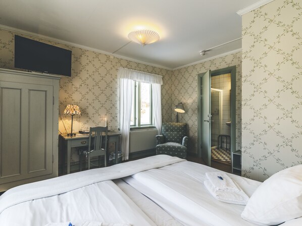 A hotel room with a bed, a desk, a chair, a radiator, and a mirror.