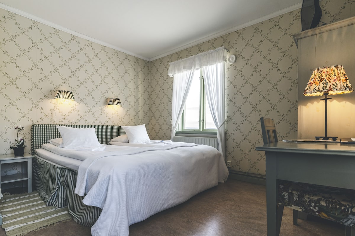A neatly arranged bedroom with a bed, bedside tables, a lamp, and a window with curtains.
