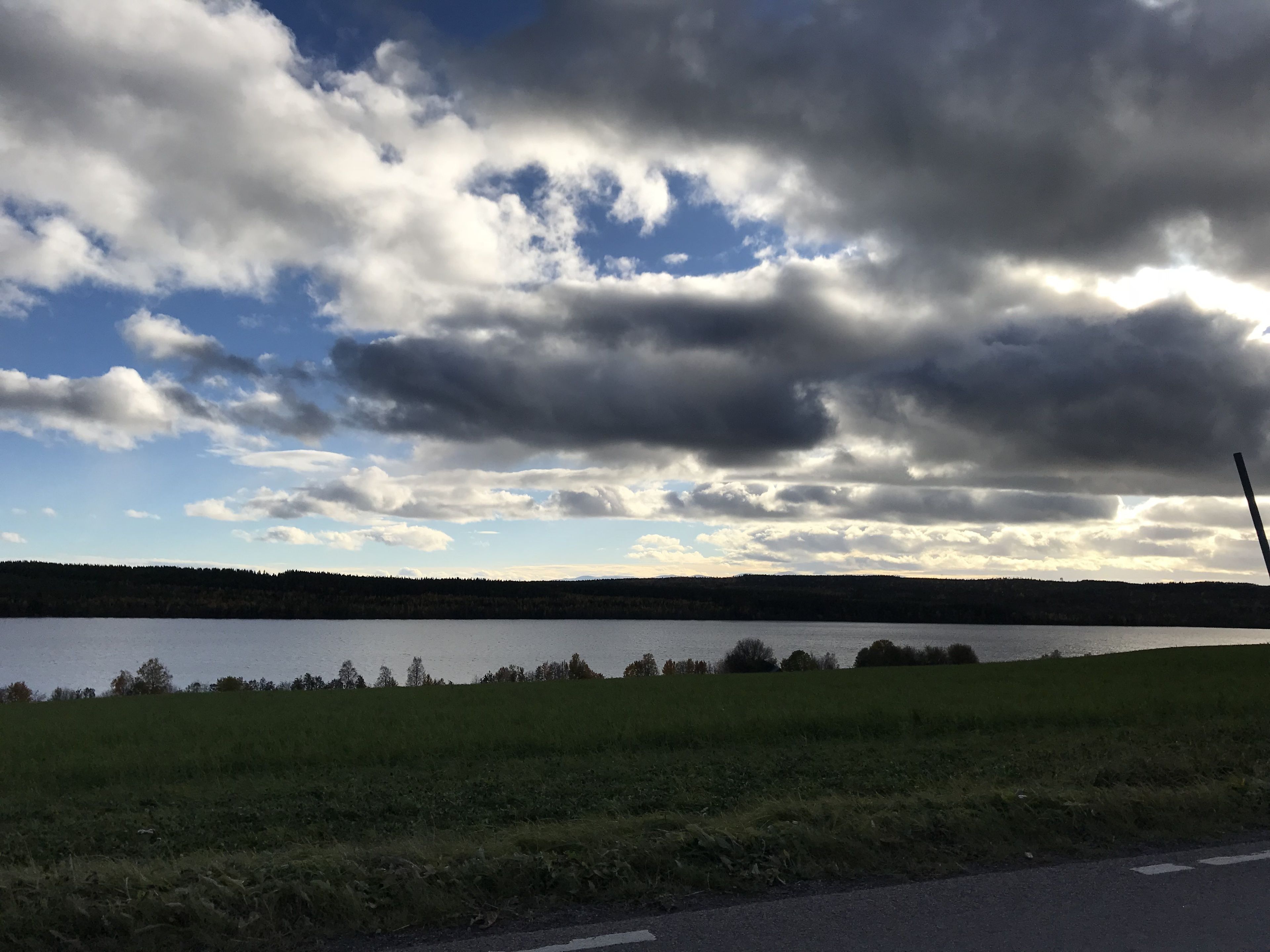 A lake with a cloudy sky and a road in the foreground.
