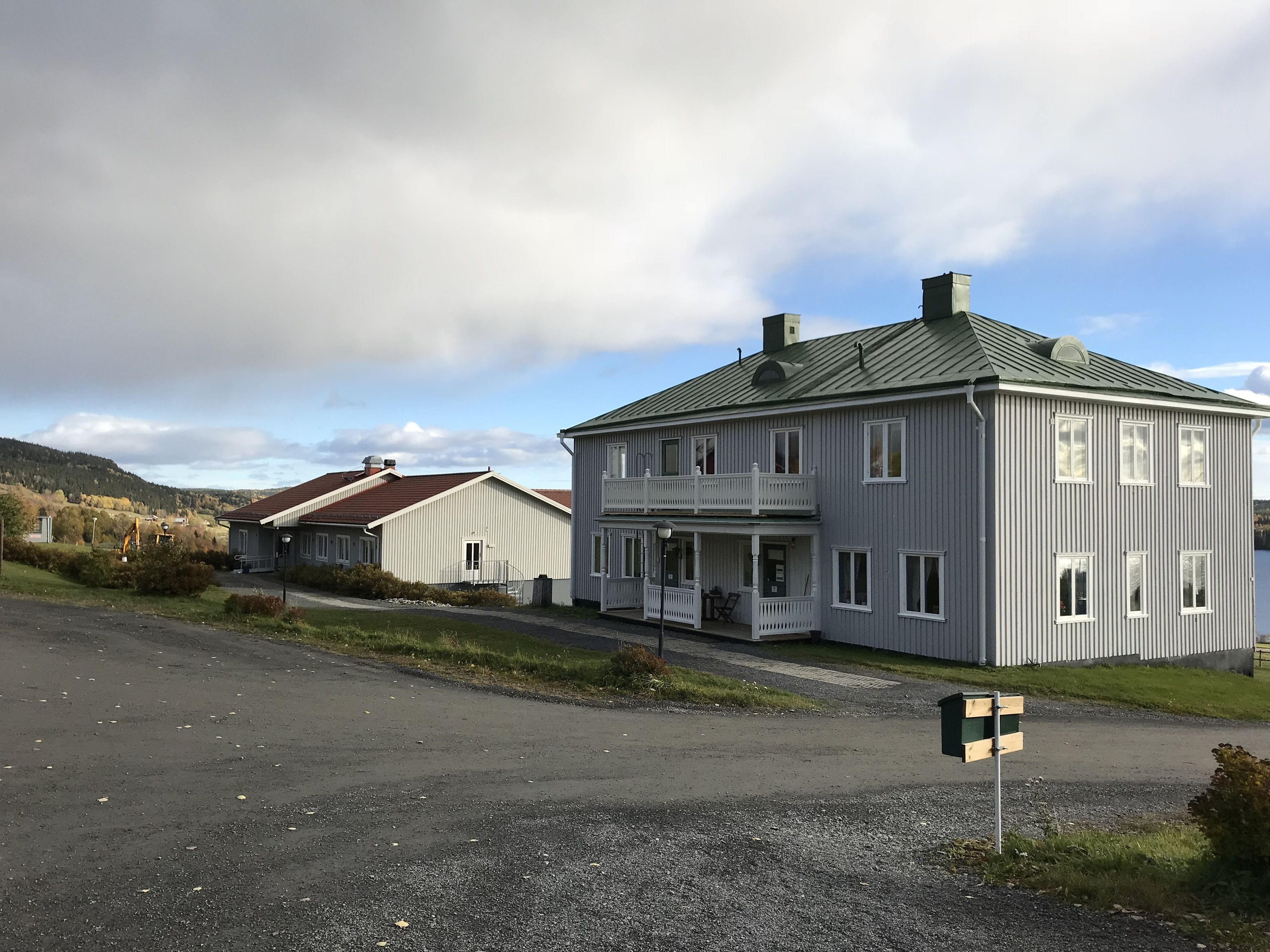A large, two-story house with a balcony, a driveway, and a gravel road in front.