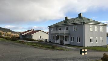 A large, two-story house with a balcony, a driveway, and a gravel road in front.