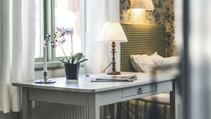 Une pièce comprenant un bureau, une orchidée en pot, une lampe et un lit avec une tête de lit à carreaux.