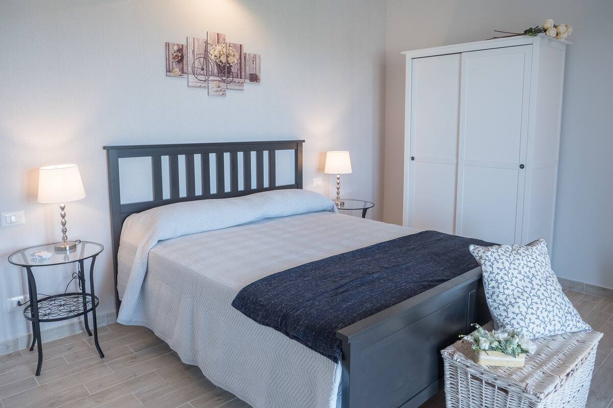 A bedroom with a bed, two bedside tables, a nightstand, a dresser, and a wall-mounted lamp.