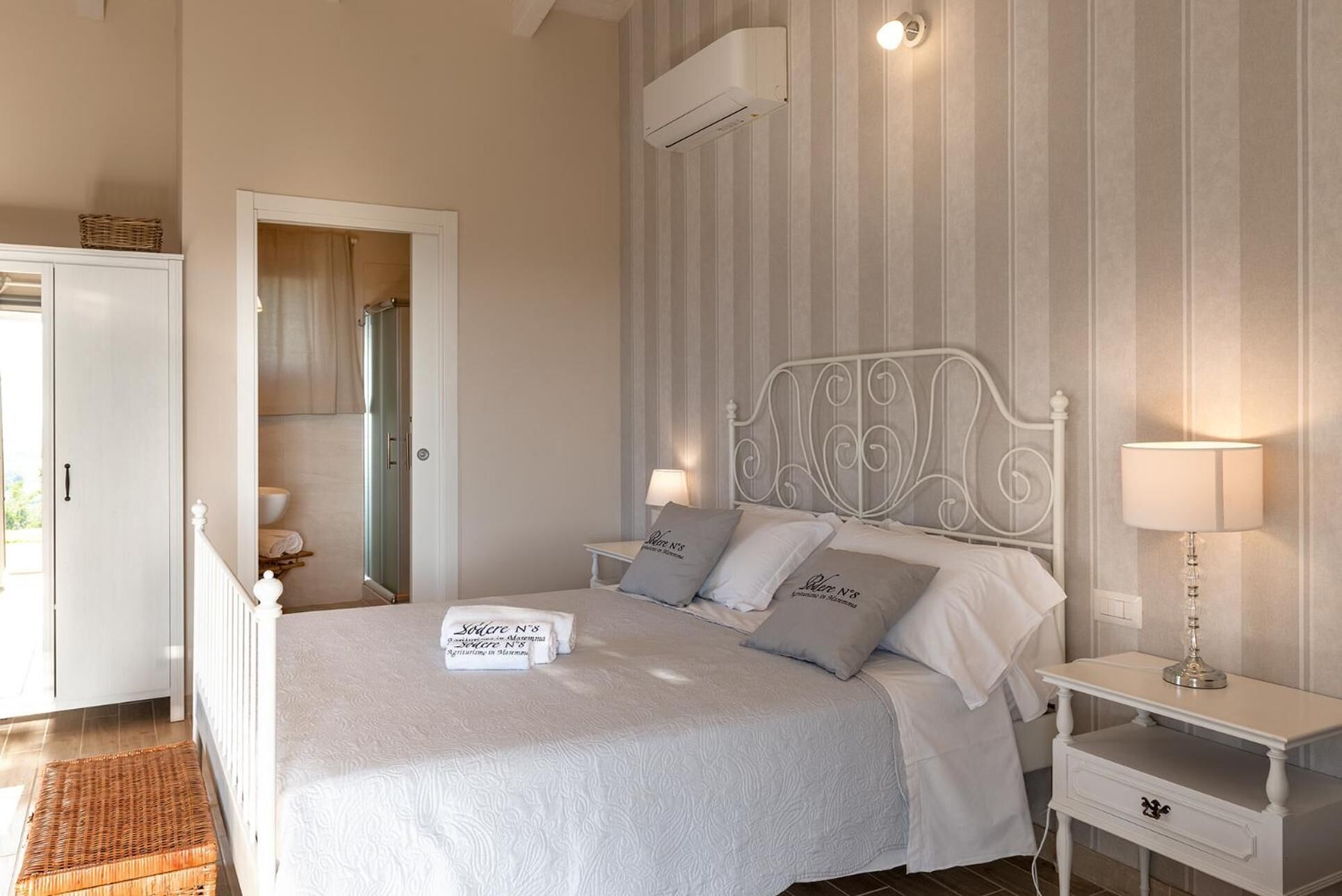 Cama bem arrumada com almofadas, mesa de cabeceira com abajur e ar-condicionado fixado na parede.