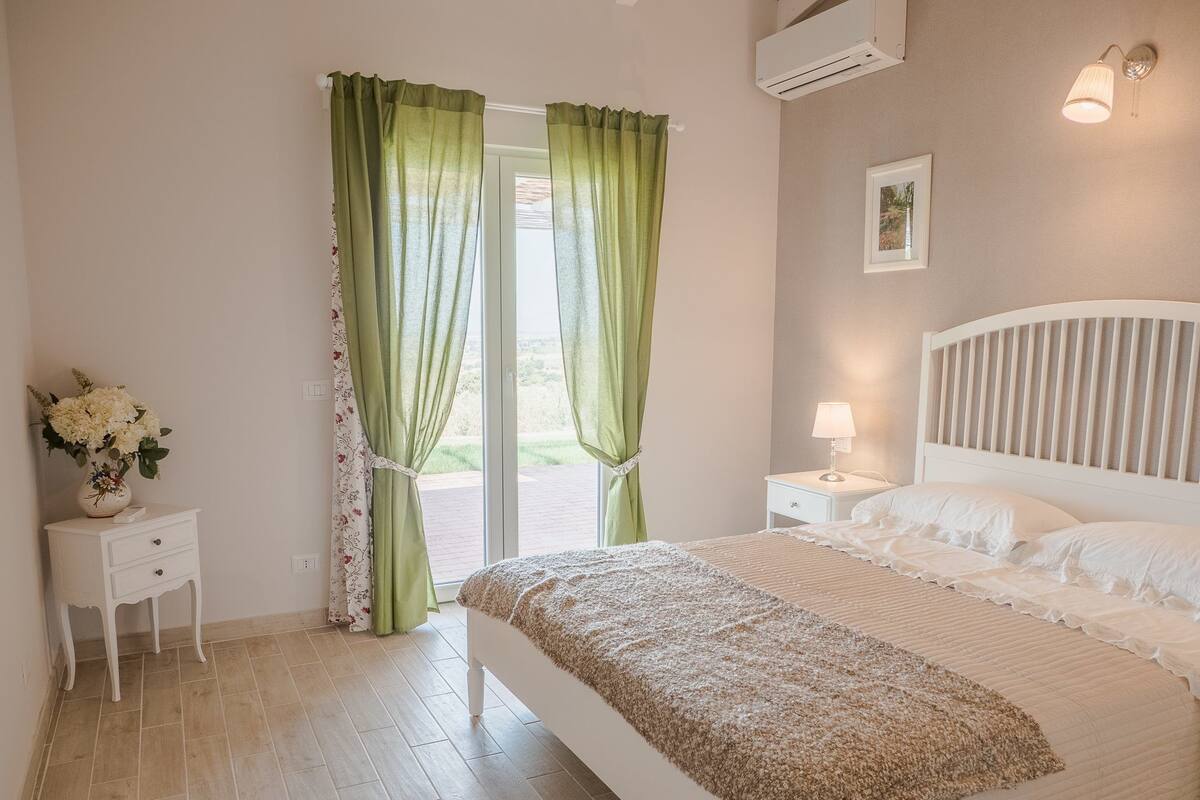 A bedroom with a bed, a nightstand, a lamp, and a window with curtains.
