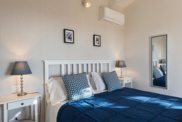 A bedroom with a white headboard, a blue bedspread, two bedside tables with lamps, and two framed pictures on the wall. - Podere n° 8 in Maremma (Magliano in Toscana)