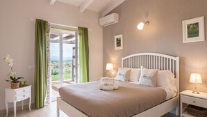 Un dormitorio con una cama, una mesita de noche, una lámpara, una ventana con cortinas y un aire acondicionado instalado en la pared.