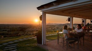 Un espacio de estar al aire libre con techo y vistas al atardecer sobre un paisaje rural.