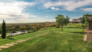 Un césped cuidado con un camino despejado que lleva a una zona de piscina, rodeada de árboles y vistas a colinas distantes.