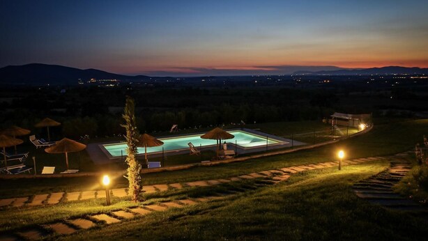 Una piscina con tumbonas y sombrillas, rodeada de un jardín ajardinado y vistas a montañas lejanas.
