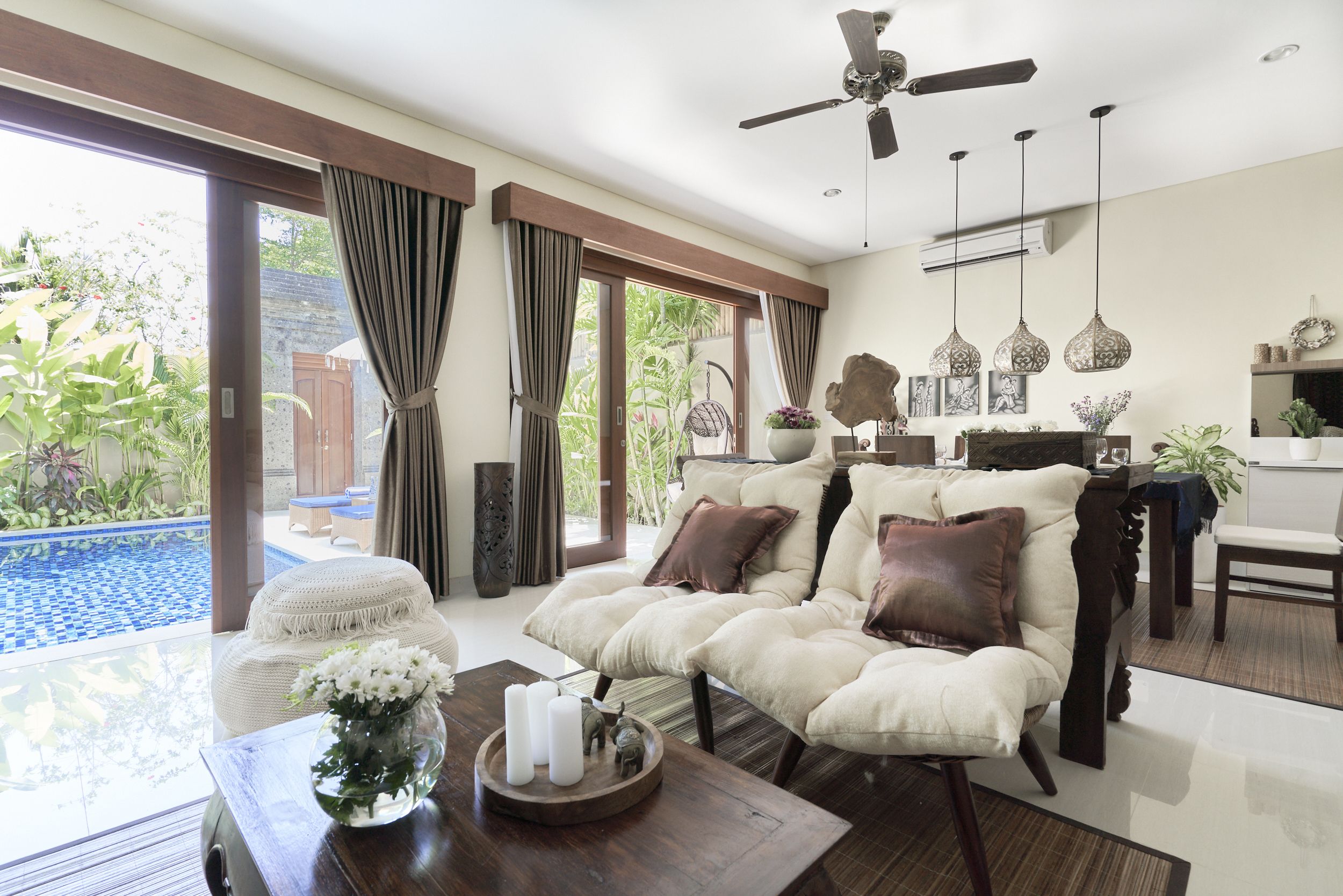 A spacious living room with a large sofa, a coffee table with decorative items, and a view of a swimming pool and garden.