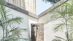 A modern outdoor shower area with a stone wall, a metal door, and potted plants. - Kubu Gajah Villas (Denpasar)