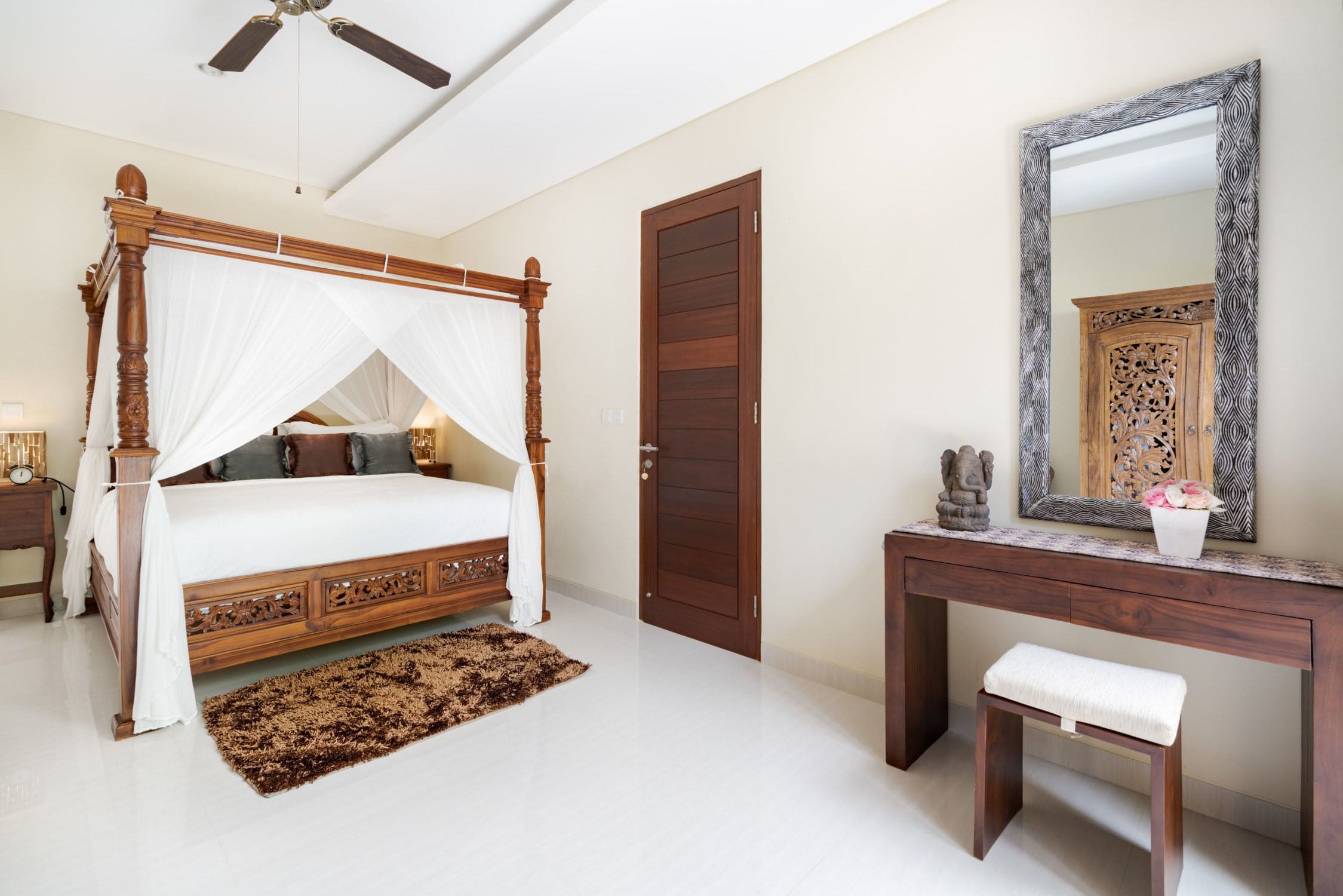A bedroom with a four-poster bed, a wooden desk, a bench, and a large mirror.