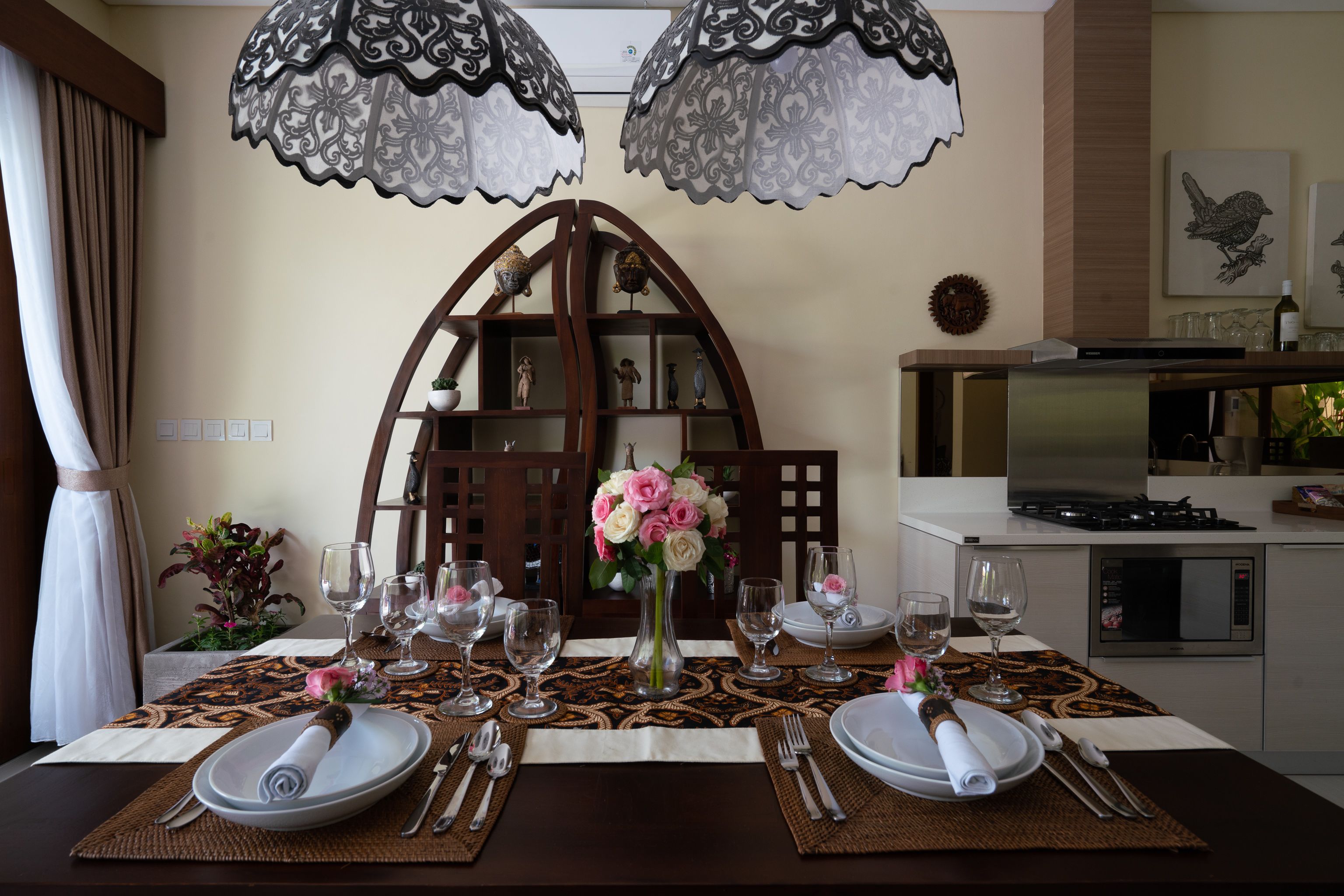 Une table à manger dressée avec des assiettes, des couverts et des verres à vin, et un vase de fleurs placé au centre.