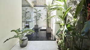 A narrow courtyard with potted plants, a wooden deck, and a stone wall. - Kubu Gajah Villas (Denpasar)