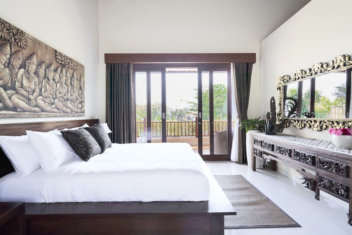 A bedroom with a large bed, a balcony with a view, and a decorative console table.