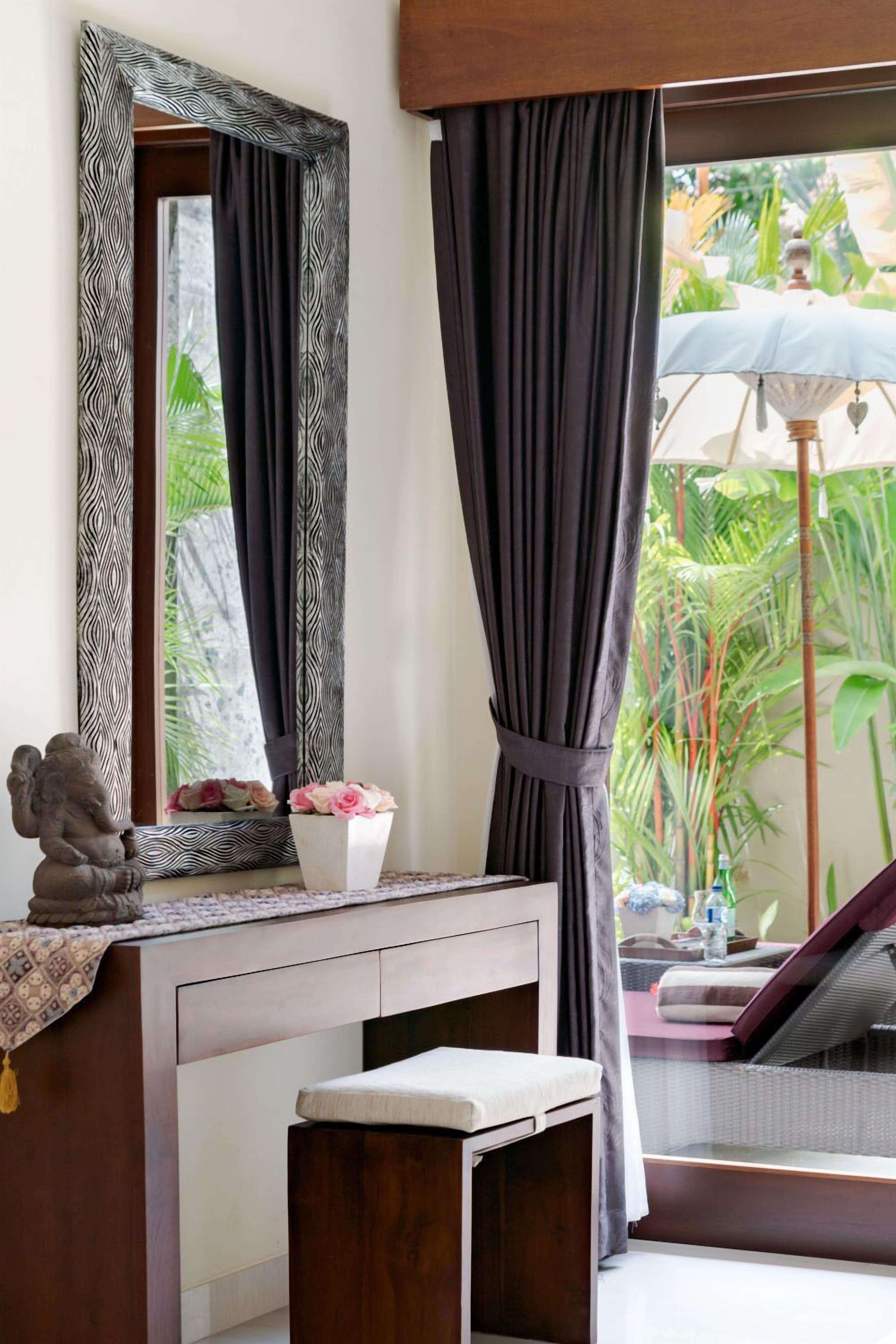 A room with a wooden desk, a mirror with a zebra pattern frame, a small statue, and a potted plant with pink flowers.