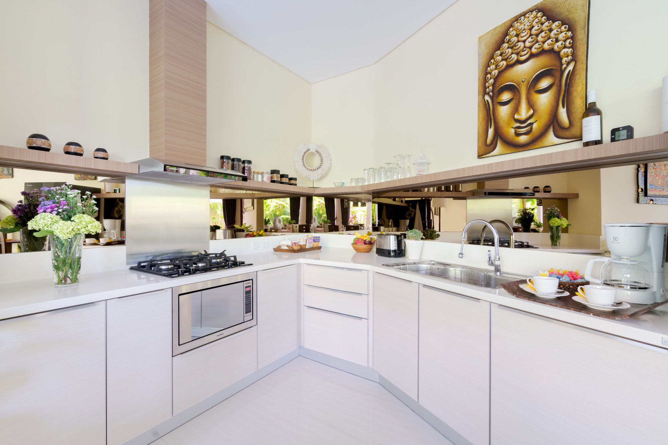Une cuisine moderne équipée d’une cuisinière à gaz, d’appareils électroménagers en acier inoxydable et ornée d’un grand tableau représentant un Bouddha.