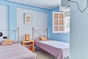 A bedroom with two single beds, a bedside table, a wall-mounted shelf, a framed picture, and a window with blinds. - Relax and sun (Santa Pola)