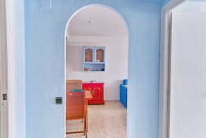 A narrow hallway with a blue wall, an arched doorway, a wooden chair, a red cabinet, and a blue sofa. - Relax and sun (Santa Pola)