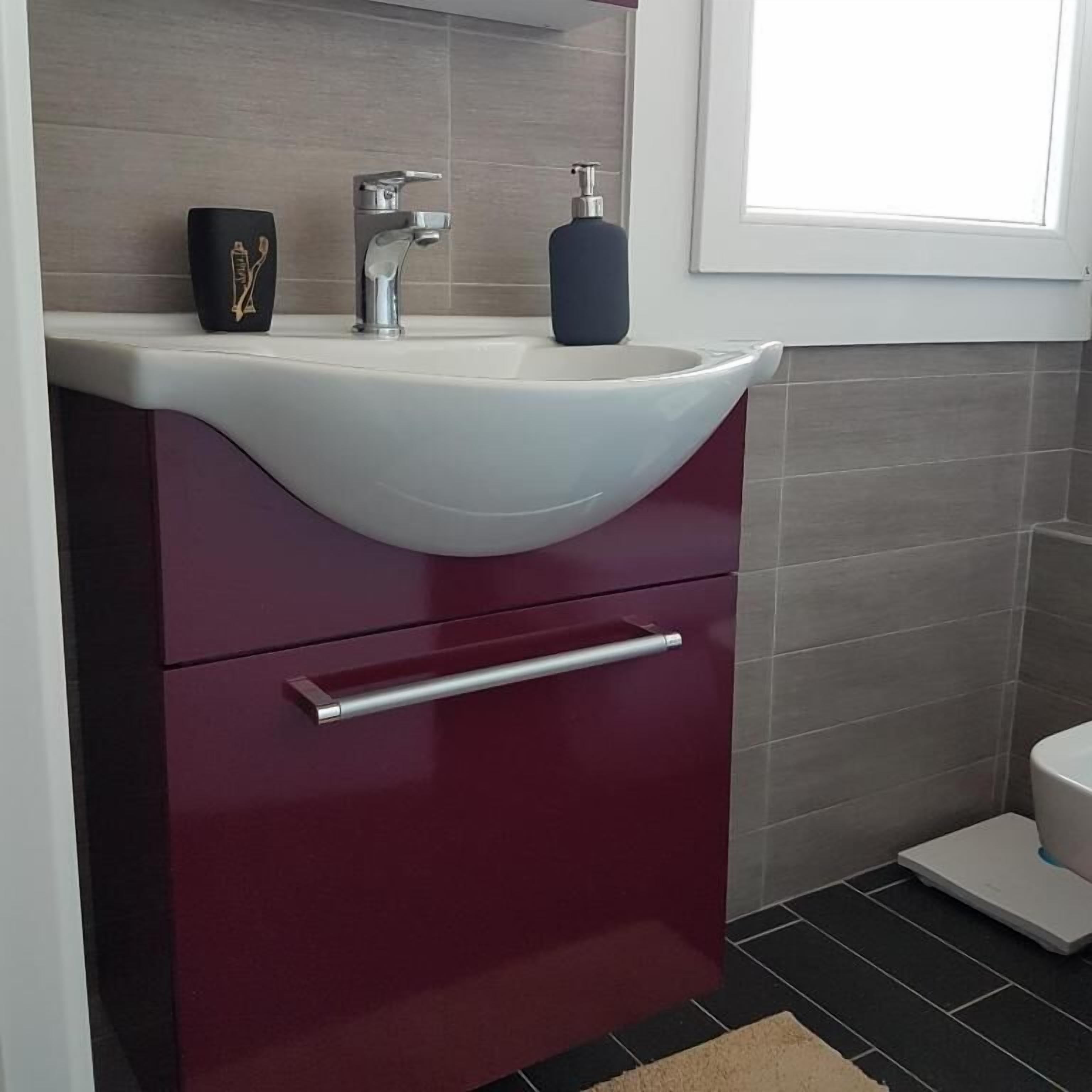 A bathroom with a white sink, a red cabinet, a black soap dispenser, and a window above the sink.