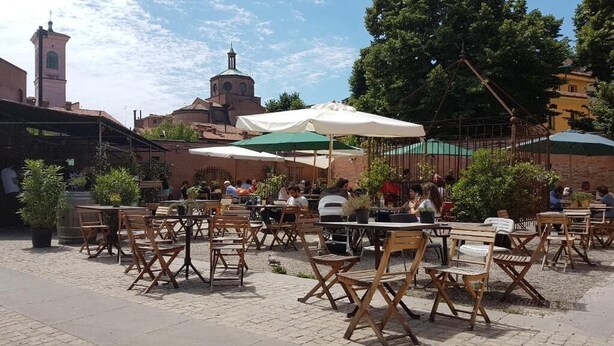 An outdoor café with wooden tables and chairs, surrounded by potted plants and umbrellas. - Il Cantuccio B&B (Bologna)