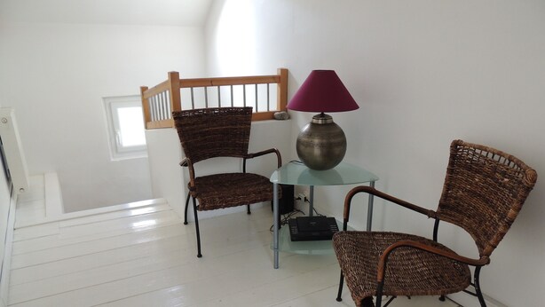 Een kamer met twee rieten stoelen, een glazen tafel, een paarse lamp en een decoratieve metalen kom.