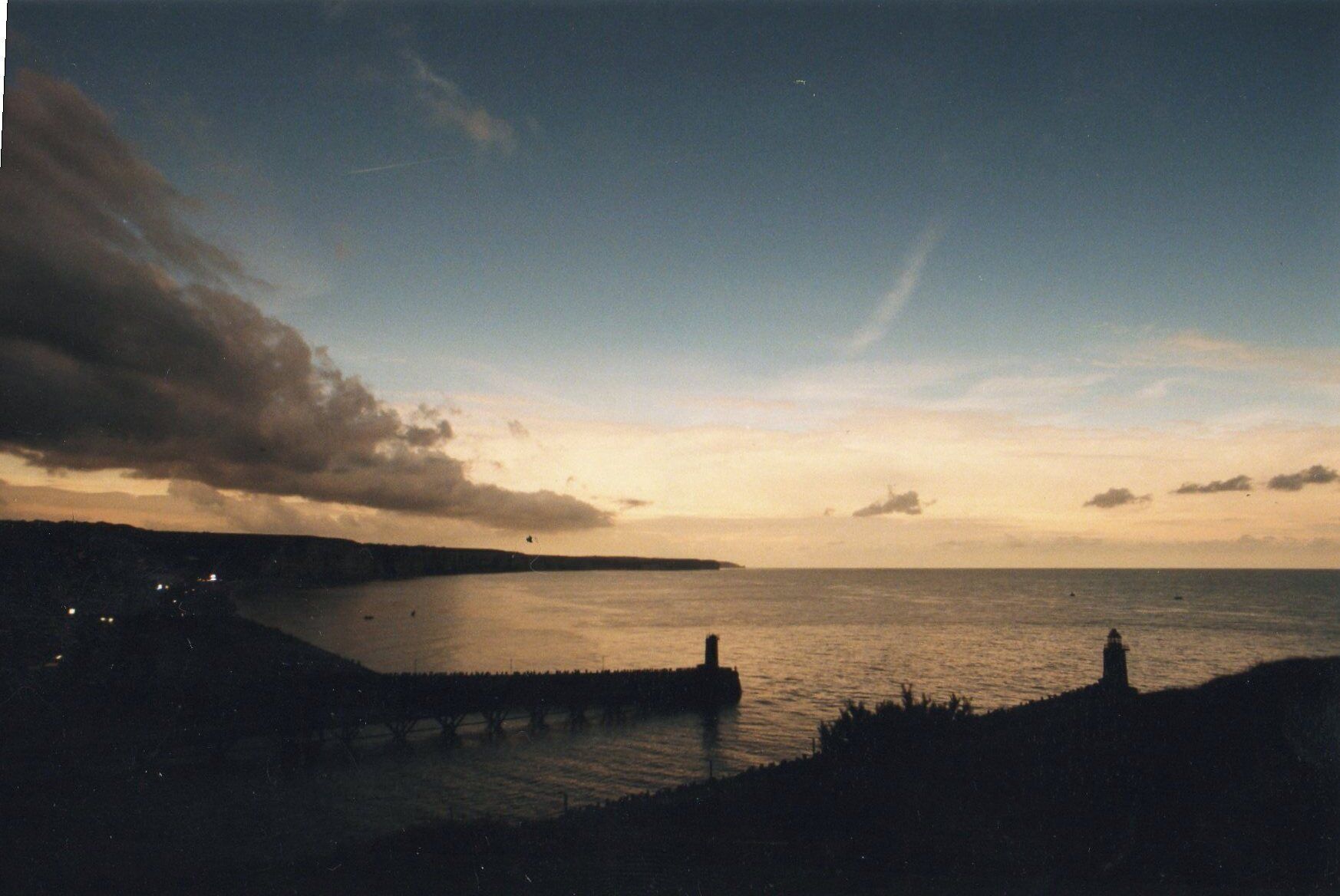 A coastal landscape with a lighthouse and a pier extending into the water.