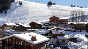 Un pueblo cubierto de nieve con edificios de madera tradicionales, un telesilla al fondo y un cielo azul despejado.