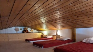 Un dormitorio abrigado en el ático, con vigas de madera, dos camas, un aparador y un adorno de oso de peluche.
