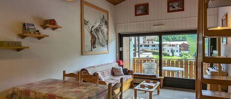 Una habitación acogedora con techo de madera, un ventanal con vistas a un paisaje verde, un sofá, una mesa y una lámpara colgante.