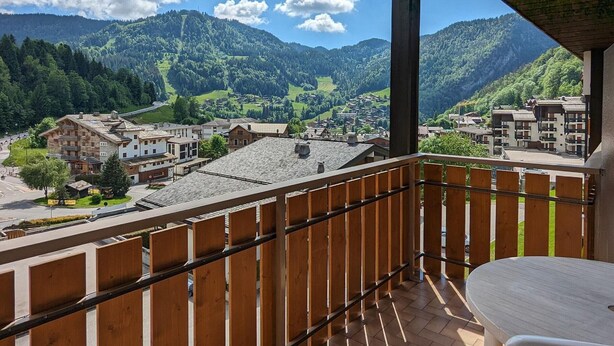 Un balcón con vistas a un pueblo de montaña, barandillas de madera y una mesa.