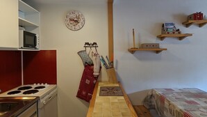 Cocina compacta con estufa, microondas y un reloj en la pared.