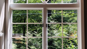 A large arched window with multiple panes, offering a view of lush greenery and trees outside.