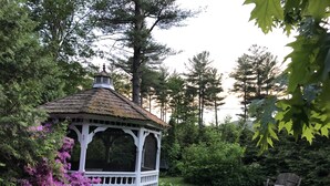 A gazebo with a thatched roof surrounded by lush greenery and flowering plants.