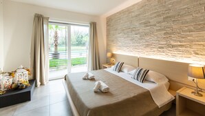 A hotel room with a large bed, a stone wall, a window with curtains, and a nightstand with a lamp. - Agriturismo Dolceluna (Milan)