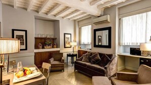 A living room with a sofa, chairs, a dining table with fruit, a lamp, and a kitchen area with a refrigerator and cabinets. - Suite Giulia 1 (Rome)