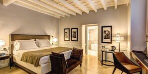 A hotel room with a large bed, a small sofa, a desk with a lamp, and framed pictures on the wall. - Suite Giulia 1 (Rome)