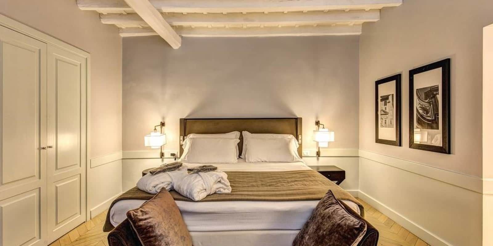 Hotellihuone, jossa on suuri sänky, kaksi yöpöytälamppua, sängynpääty ja seinällä olevia kehystettyjä kuvia.