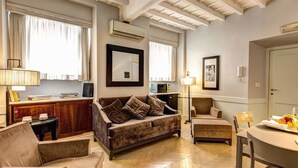A cozy living room with a sofa, armchairs, a dining table with fruit and glasses, and a TV. - Suite Giulia 1 (Rome)