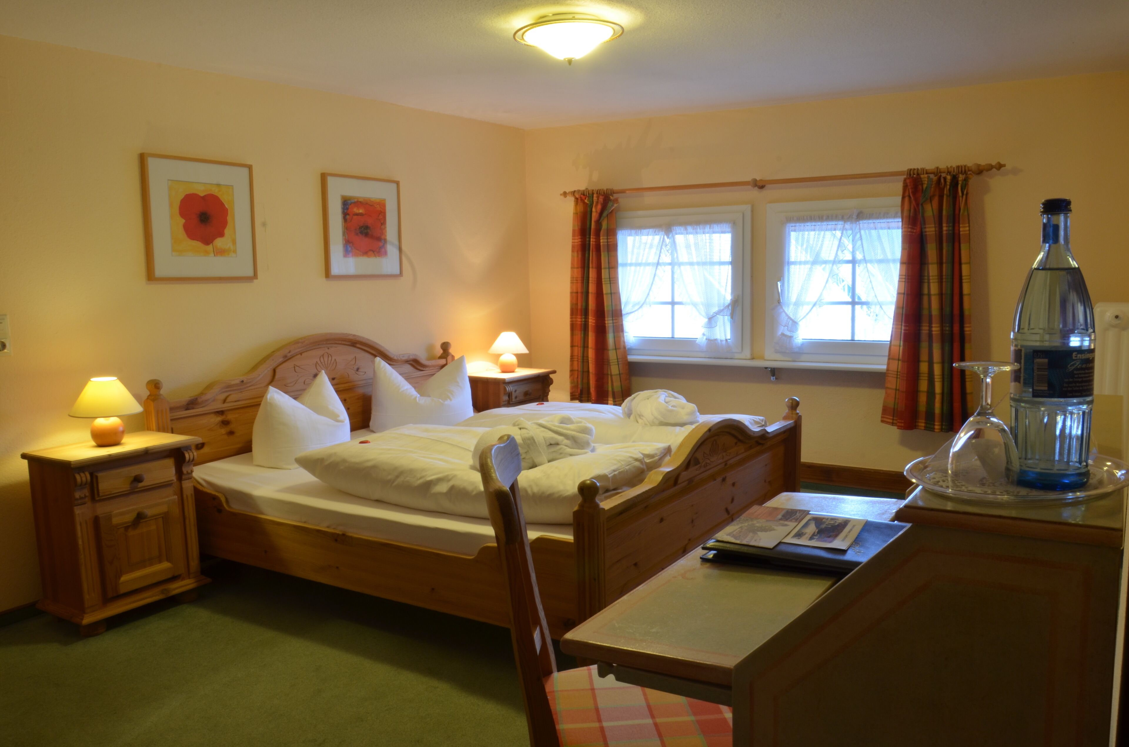 A bedroom with a wooden bed, bedside tables with lamps, a window with curtains, and a bedside table with a bottle and glass.