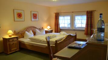 A bedroom with a wooden bed, bedside tables with lamps, a window with curtains, and a bedside table with a bottle and glass.