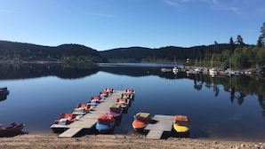 Un lago tranquilo con un muelle de madera que se adentra en el agua, bordeado por botes remos de colores.